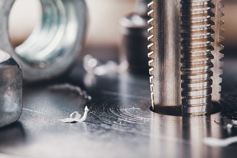 Detailaufnahme von einem Gewindeschneider mit Spänen auf einer Metalloberfläche.