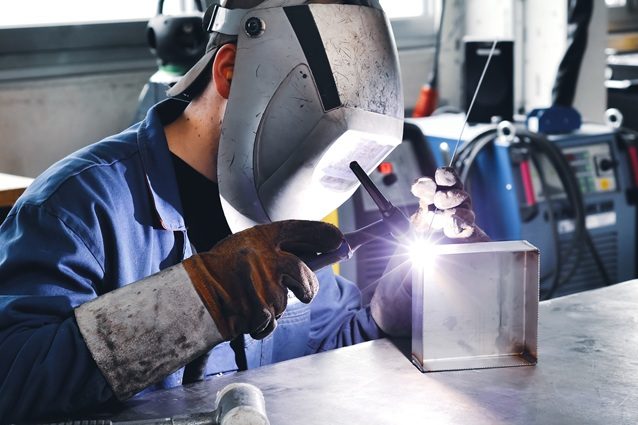 Ein Mensch schweißt an einem Metallblock in einer Werkstatt.